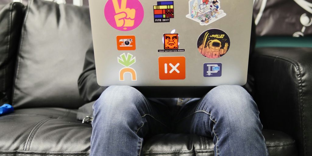man using silver MacBook sitting on black leather sofa